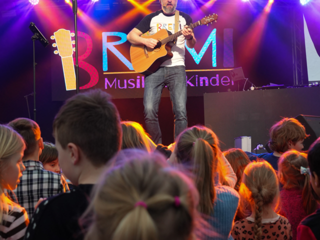 Bremi steht mit der Gitarre auf der Bühne